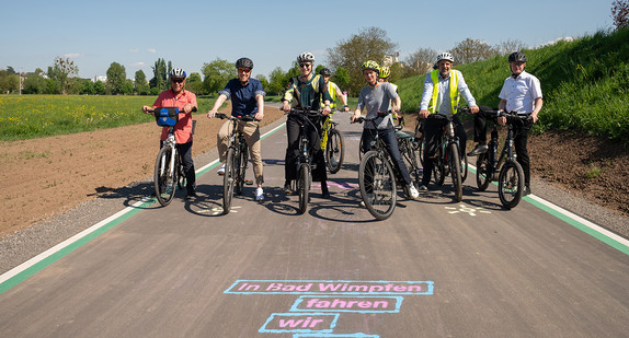 Radfahrer mit Helm stehen auf dem neuen Radweg in Bad Wimpfen. Auf dem Boden steht in blau und pink: "In Bad Wimpfen fahren wir Rad"